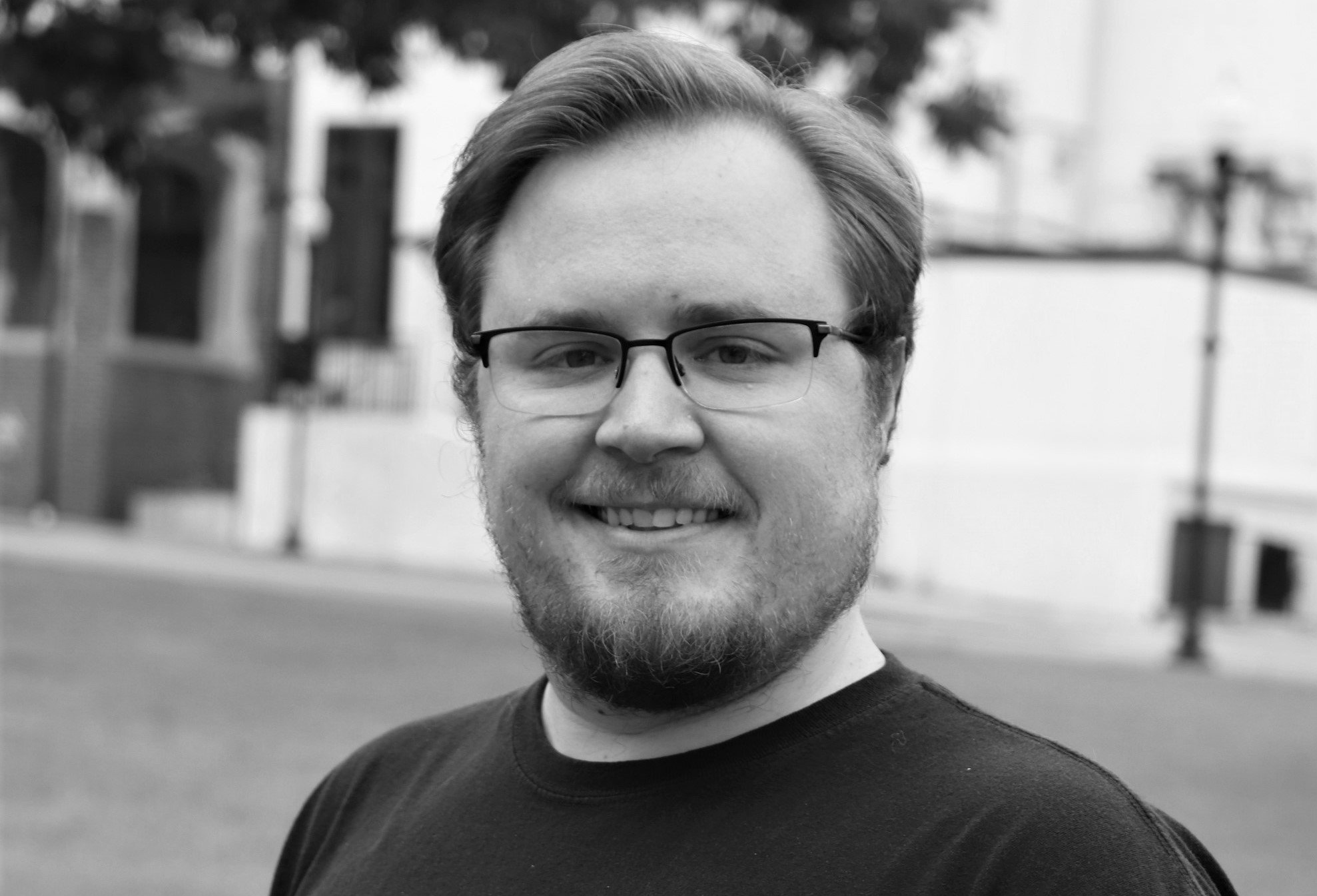 A smiling man with a beard and glasses in a black t-shirt for the Elbert Theatre Foundation.