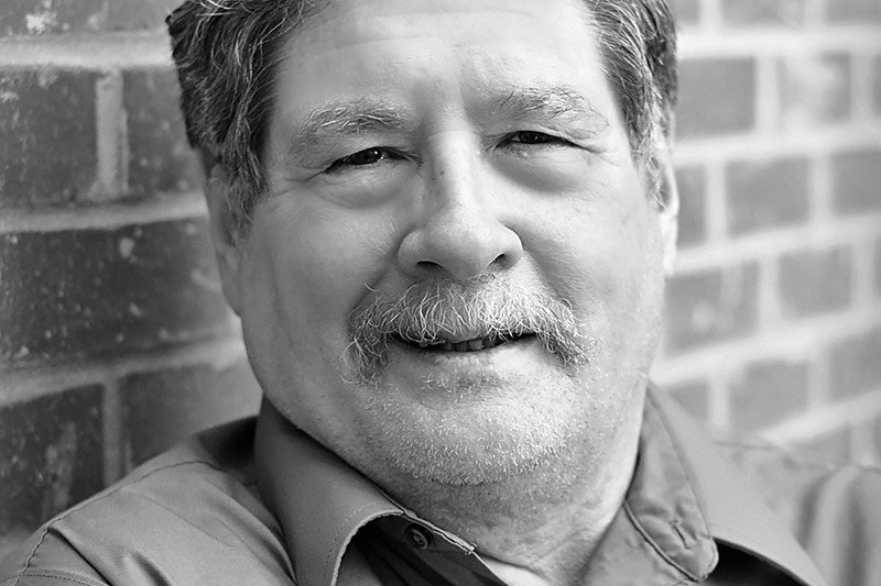 Black and white portrait of a smiling older man with a mustache, reminiscent of the figures once honored by the Elbert Theatre Foundation.
