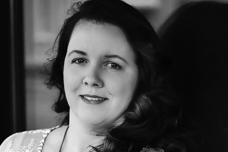 A black and white close-up portrait of a woman looking directly at the camera, associated with the Elbert Theatre Foundation.