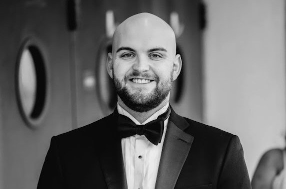 A smiling man with a shaved head and a beard, wearing a tuxedo with a bow tie for the Elbert Theatre Foundation.